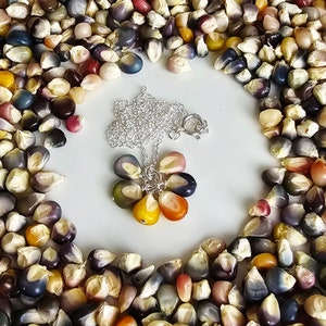 May include: A silver chain necklace with a pendant made of colorful corn kernels. The pendant is shaped like a flower with six petals. The necklace is surrounded by a border of colorful corn kernels.