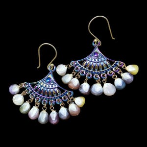May include: A pair of iridescent earrings with a fan-shaped design and multiple dangling beads. The earrings are made of metal and have a gold finish.