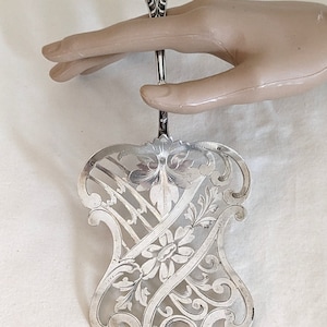 May include: A silver cake server with an ornate, pierced design. The handle is decorated with a floral motif.