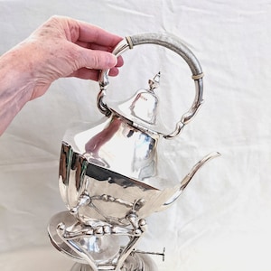 May include: A silver teapot with a decorative handle and a burner base. The teapot is octagonal in shape and has a spout and lid.