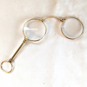 Op de afbeelding: Een verguld vergrootglas met een ronde handgreep en een scharnierende, vouwbare lens.