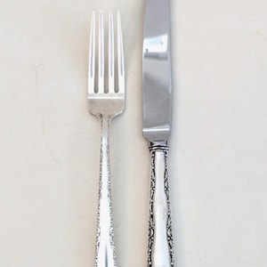 May include: A silver fork and knife with ornate handles. The knife has an engraved monogram.