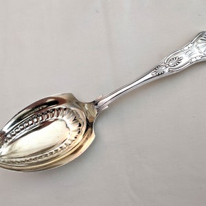 May include: A silver serving spoon with an ornate handle and a decorative, oval-shaped bowl.