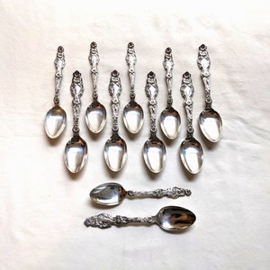 Puede incluir: Juego de doce cucharaditas de plata con mangos adornados. Las cucharas tienen un diseño clásico y son perfectas para servir té o café.