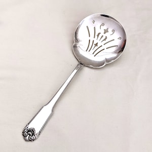 以下が含まれることがあります： 装飾的な透かし模様が施された銀製のサービングスプーン。スプーンは、丸みを帯びたボウルに花柄が施され、長く細いハンドルが付いています。