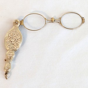 May include: A gold-toned folding eyeglass with an ornate floral design on the handle.