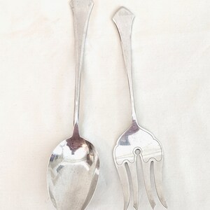 May include: A silver serving spoon and fork with ornate handles. The spoon has a rounded bowl and the fork has three tines.