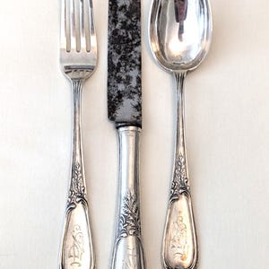 May include: A set of three silver-plated utensils with ornate handles. The fork, knife, and spoon have engraved initials on the handles.