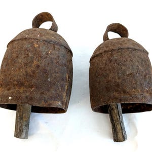 K&ouml;nnte beinhalten: Zwei antike, rustikale Metallglocken mit einem verwitterten, rostbraunen Finish. Jede Glocke hat einen Holzkl&ouml;ppel und eine Schlaufe zum Aufh&auml;ngen. Die Glocken sind wahrscheinlich Vintage und eignen sich f&uuml;r Bauernhaus- oder rustikale Dekorationen.