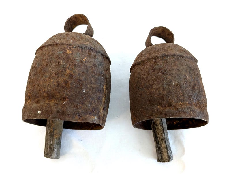 K&ouml;nnte beinhalten: Zwei antike, rustikale Metallglocken mit einem verwitterten, rostbraunen Finish. Jede Glocke hat einen Holzkl&ouml;ppel und eine Schlaufe zum Aufh&auml;ngen. Die Glocken sind wahrscheinlich Vintage und eignen sich f&uuml;r Bauernhaus- oder rustikale Dekorationen.
