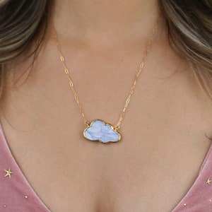 May include: A gold chain necklace with a light blue cloud-shaped pendant. The cloud has a marbled pattern and a gold outline.