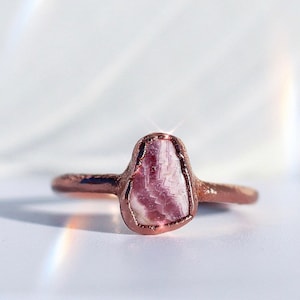 May include: A rose gold ring with a pink and white gemstone set in the center.