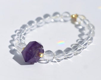 May include: A bracelet made of clear quartz beads with a single, faceted amethyst bead in the center. The amethyst bead is a deep purple color and is surrounded by gold accents.