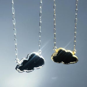 May include: Two silver and gold necklaces with black cloud pendants. The necklaces have a delicate chain link design.