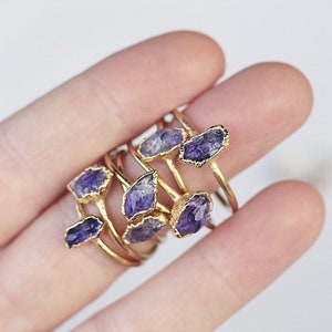 May include: A set of gold rings with purple amethyst stones. The rings are stacked on top of each other and are worn on a finger.