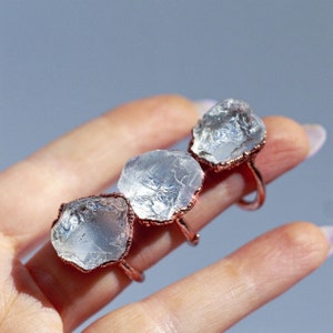 May include: Three clear quartz crystal rings with copper wire settings. The rings are on a hand.