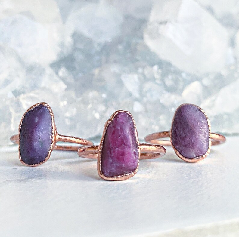 Puede incluir: Tres anillos hechos a mano con piedras preciosas moradas en bruto de forma ovalada, engastadas en metal color cobre. Las piedras preciosas var&iacute;an en tonos de morado y est&aacute;n engastadas en bandas finas y delicadas.