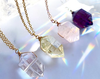 May include: Four gold necklaces with different colored crystal pendants. The pendants are shaped like a point and are clear, pink, yellow, and purple.