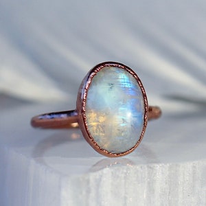 May include: A rose gold ring with a white moonstone oval cabochon.