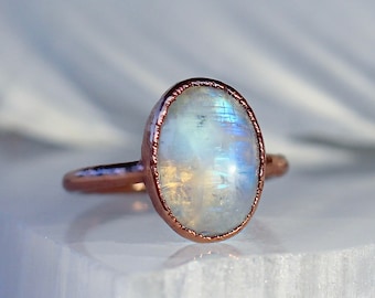 May include: A rose gold ring with a white moonstone oval cabochon.