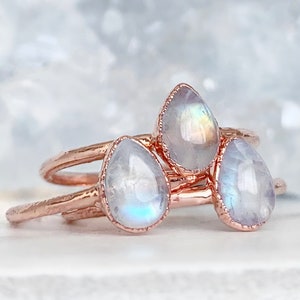 May include: Three rose gold rings with teardrop-shaped moonstone gemstones. The rings are stacked on top of each other.