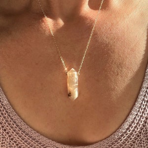 Peut inclure: Un collier en chaîne dorée avec un pendentif en cristal brun clair. Le pendentif a la forme d'une longue pointe fine.