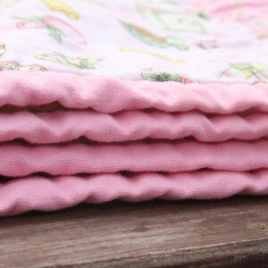 Puede incluir: Una manta de beb&eacute; rosa doblada en capas, mostrando la tela suave y texturizada.