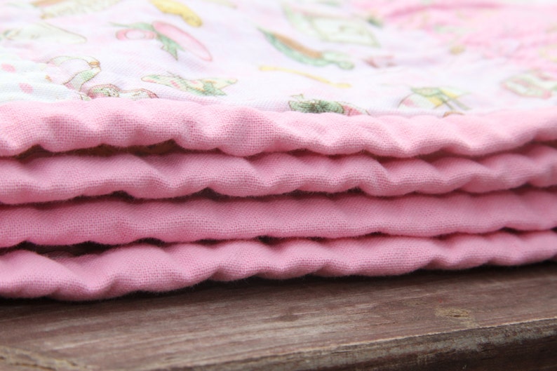 Puede incluir: Una manta de beb&eacute; rosa doblada en capas, mostrando la tela suave y texturizada.