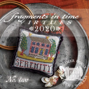 May include: A small, white cross-stitch pillow with a red house and green trees. The pillow is on a silver tray with the words "Serenity" and "No. two" in black lettering. The words "Fragments in Time" and "Virtues 2020" are in the background.