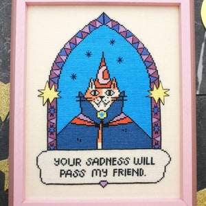 Könnte beinhalten: Eine Kreuzstich-Stickerei eines Katers, der einen Zaubererhut und eine Robe trägt. Die Katze befindet sich in einem blauen Torbogen mit Sternen und dem Text "Your sadness will pass my friend."
