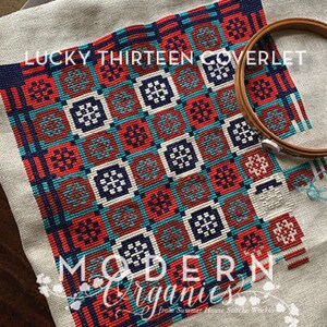 Pode incluir: Um padrão de ponto cruz com um design geométrico em tons de vermelho, azul e branco. O padrão é intitulado "Lucky Thirteen Coverlet" e é de "Modern Organics".