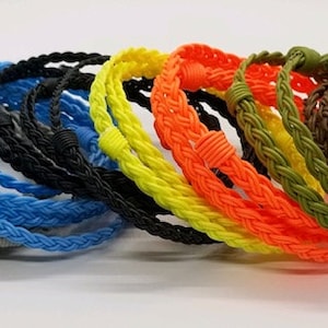 May include: A collection of braided bracelets in various colors, including gray, blue, yellow, orange, and green. The bracelets are made of a woven cord material.