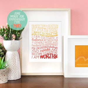 May include: A framed print with a pink background and white frame. The print features a text-based design with the words "Some Words for Enneagram Type Two" in a circle at the top. The text below reads "My affection & devotion can be healing & nourishing not only for others, but also for myself. I want to make the world more compassionate. I can cultivate a balance between my others' needs and nurture independence. My uncensored feelings and needs are welcome & essential. I am worthy."