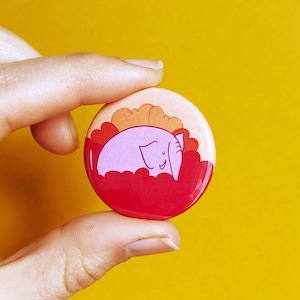 May include: A pink elephant with a smile is sleeping on a red and orange cloud. The image is a button.