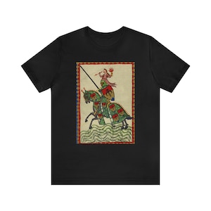 May include: Black t-shirt featuring a medieval illustration of a knight on horseback. The artwork depicts a knight in armor with a lance, riding a green horse with red and green accents. The background is a cream color with a red border.