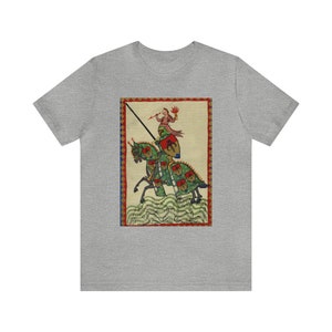 May include: A gray t-shirt featuring a medieval illustration of a knight on horseback. The artwork depicts a knight in armor with a lance, riding a horse with green and red accents. The design is framed with a red and blue border.