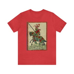 May include: Red t-shirt featuring a medieval illustration of a knight on horseback. The artwork depicts a knight in armor with a lance, riding a green horse with red and green accents. The background is a cream color with a decorative border.