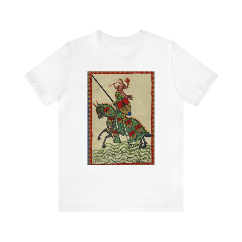May include: White t-shirt featuring a medieval illustration of a knight on horseback. The artwork depicts a knight in red and green armor with a lance, riding a green horse with red and green accents. The background is beige with a red border.