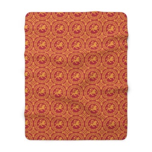 May include: A red and gold blanket with a repeating pattern of circular medallions featuring a lion rampant. The blanket has a soft, plush texture and a decorative, medieval-inspired design.