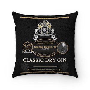 Op de afbeelding: Zwart vierkant kussen met een goud en wit label ontwerp. Het label leest "Qui-Gon Distillery" en "Classic Dry Gin". Het kussen heeft een getextureerde uitstraling en bevat de tekst "Coruscant Cut".