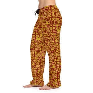 May include: Burgundy and gold pajama pants with a repeating pattern of heraldic designs. The pants have a drawstring waist and a relaxed fit. The pattern includes lions, griffins, and other medieval-style motifs.