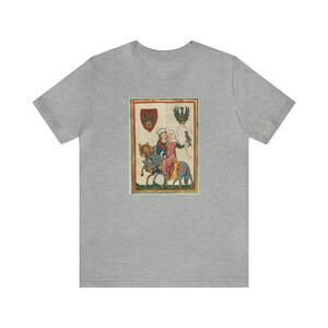 May include: A heather gray t-shirt featuring a medieval illustration. The artwork depicts two figures on horseback, with a bird and heraldic crests. The illustration is framed with a red and gold border.