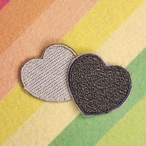 May include: Two heart-shaped patches. One is light gray with a textured pattern and a silver border. The other is dark gray with a similar border. They rest on a rainbow-striped background.