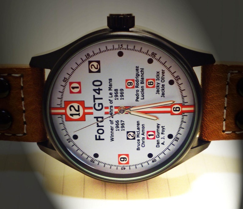 May include: A white watch face with black hands and black markings. The watch face has the text "Ford GT40" and "Winner of 24hrs of Le Mans" with the years 1966, 1967, 1968, and 1969. The watch face also has the names of the drivers who won the race in those years.