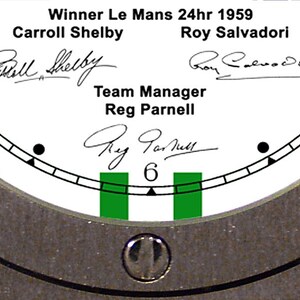 May include: Close-up of a watch face with the text "Winner Le Mans 24hr 1959" and the names Carroll Shelby, Roy Salvadori, and Reg Parnell. The watch face is white with black markings and green accents, surrounded by a silver metal bezel.