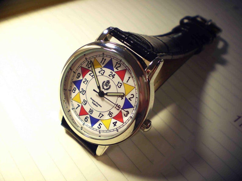 May include: A silver wristwatch with a black leather band. The watch face has a white background with a colorful circular design and black hands. The numbers on the watch face are in black and white.