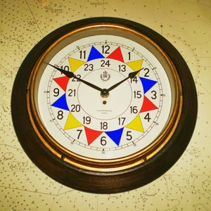Peut inclure: Une horloge ronde à cadre en bois avec un cadran blanc et une bordure dorée. L'horloge a une aiguille des heures et des minutes noire et une aiguille des secondes rouge. Le cadran est divisé en 12 sections, chacune d'une couleur différente : rouge, jaune, bleu et blanc. L'horloge comporte également les chiffres de 1 à 12 autour du bord, ainsi que les mots "Aiton & Manvers, Derby".
