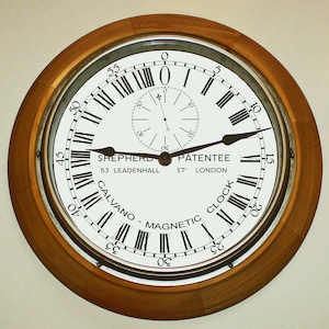 May include: A round, wooden-framed clock with a white face and black Roman numeral markings. The clock face also includes the text "SHEPHERD PATENTEE 53 LEADENHALL ST LONDON" and "CALVANO - MAGNETIC CLOCK".