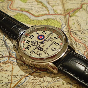 May include: A black leather wristwatch with a silver face and white hands. The face has a red and white target design and the text "ROLLS ROYCE DH.98 Mosquito".