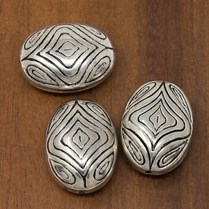 May include: Three silver oval-shaped beads with a geometric design. The beads have a raised diamond pattern with a swirl design around the edges.